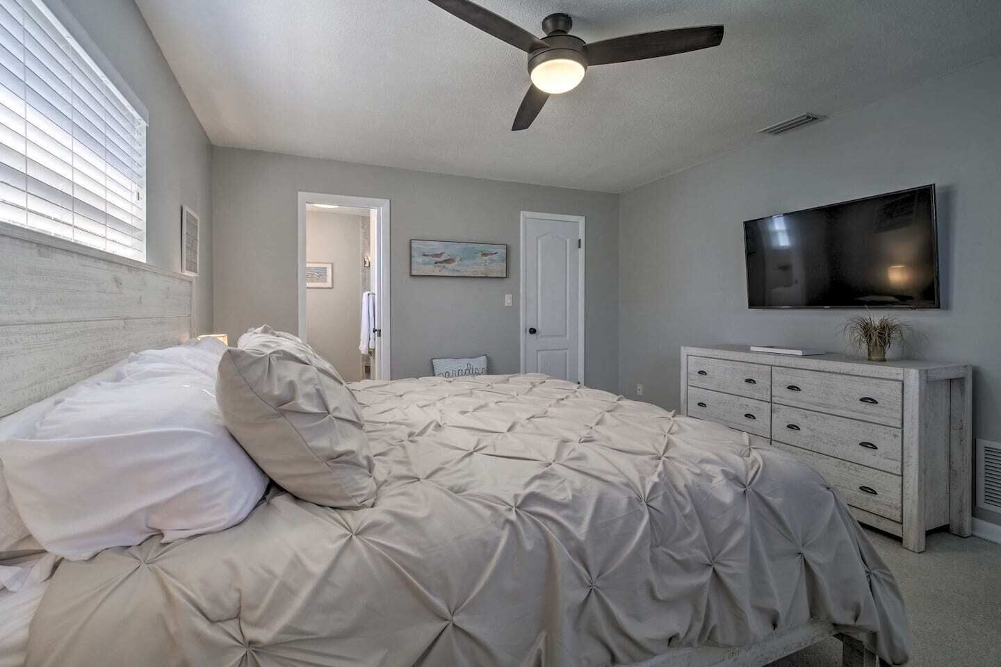 A bedroom with a bed, a dresser, a ceiling fan, a TV, and a door.