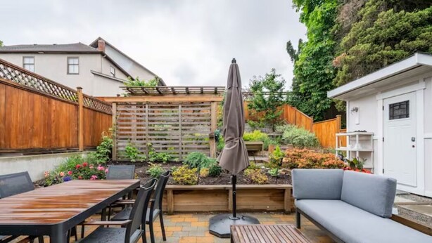 A patio area with a wooden table and chairs, a grey sofa, and a wooden deck. - Private Suite!! Convenient location for Commuters, Essential Workers and Trades! (New Westminster)