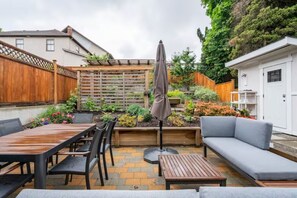 Un espace patio aménagé avec une table et des chaises en bois, un canapé gris et une terrasse en bois.