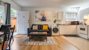 A compact living space with a sofa, coffee table, washing machine, and kitchenette. - Private Suite!! Convenient location for Commuters, Essential Workers and Trades! (New Westminster)