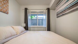 A hotel room with a bed, a window with curtains, a lamp, and a painting on the wall. - Private Suite!! Convenient location for Commuters, Essential Workers and Trades! (New Westminster)
