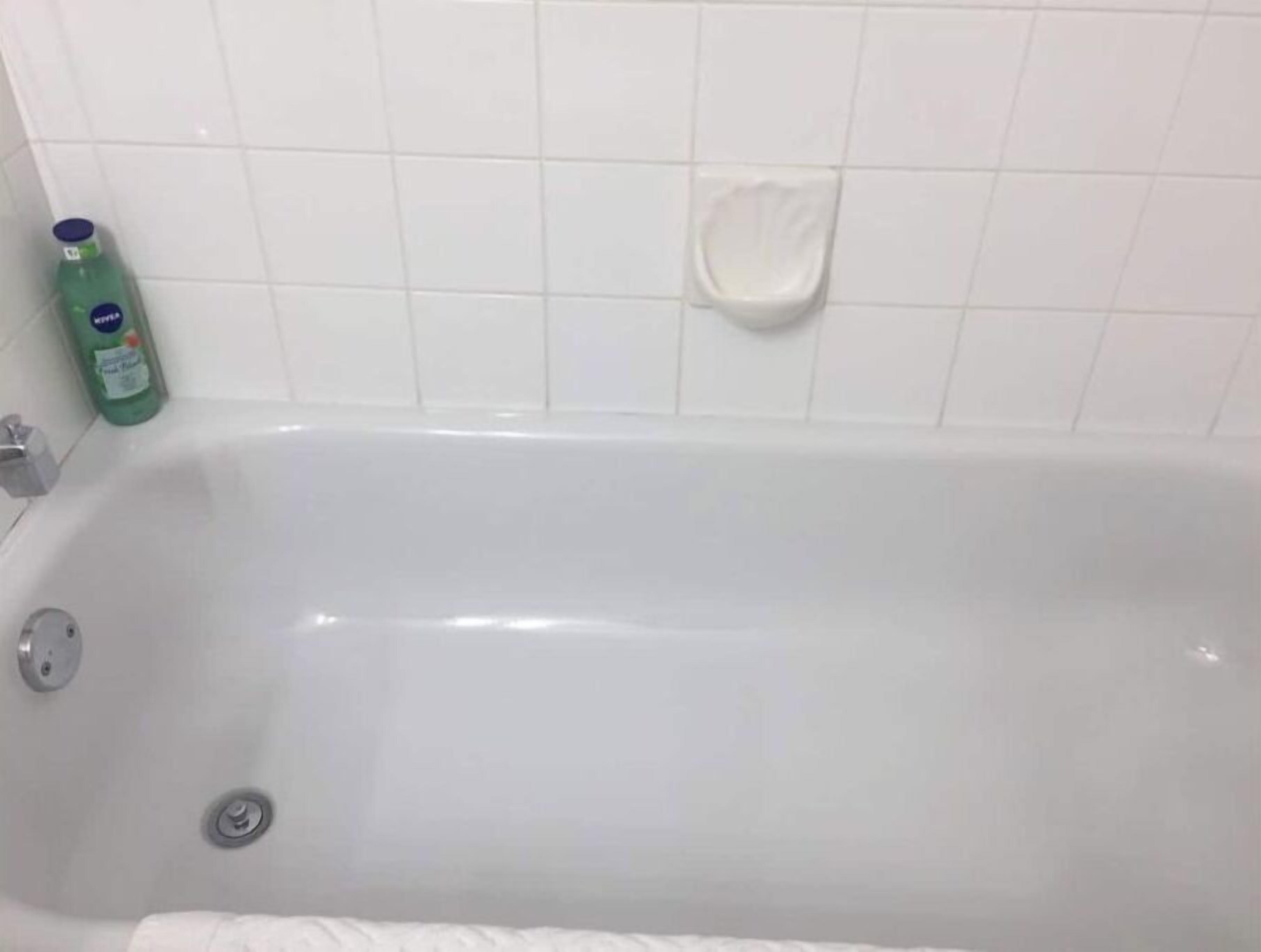 A white bathtub with a green bottle of shampoo and a soap dish on the wall.
