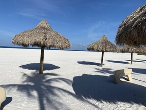 En strand med stråparasoller og en plastikstol.