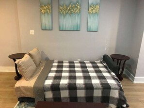 Een slaapkamer met een geruite bedspreiding, twee nachtkastjes, een bankje en drie aan de muur hangende schilderijen.