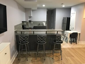 A modern kitchen with a bar area, a dining table, and a TV mounted on the wall.