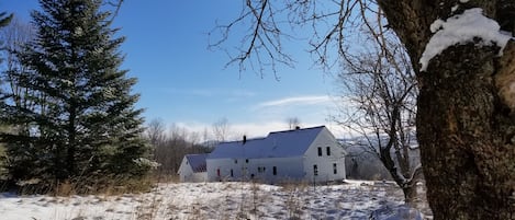 Ein großes, weißes Gebäude mit geneigtem Dach, umgeben von schneebedecktem Boden und spärlicher Vegetation.