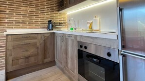 A modern kitchen with a brick wall, wooden cabinets, stainless steel appliances, and a white countertop.