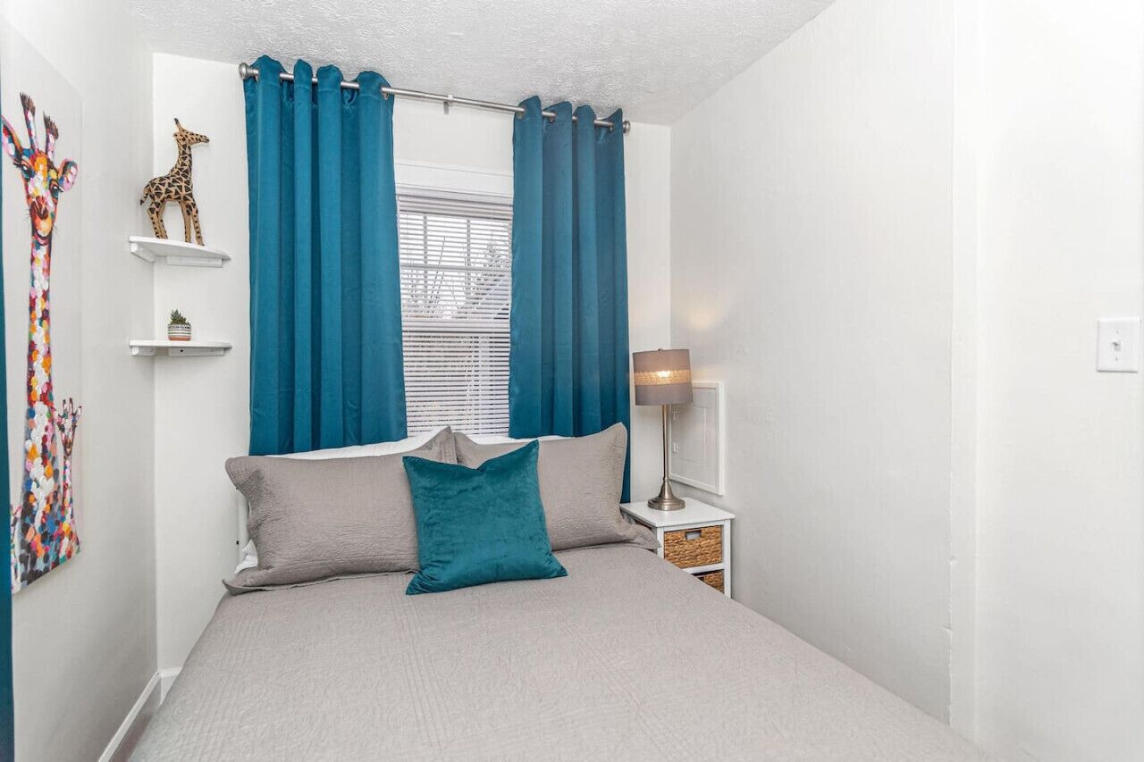 Een slaapkamer met een bed, teal gordijnen, een girafdecoratie en een lamp.