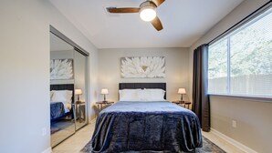 Una camera da letto con un letto grande, due comodini con lampade, una ventola a soffitto, un'ampia finestra con tende e uno specchio a parete.