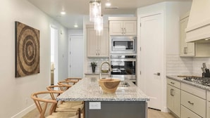 A modern kitchen with a granite countertop, stainless steel appliances, and a central island with a sink. - Camelot by RedAwning (St. George)