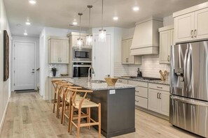 A modern kitchen with a central island, stainless steel appliances, and wooden bar stools. - Camelot by RedAwning (St. George)