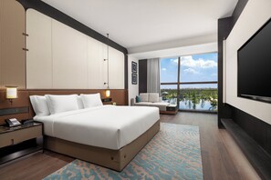 Ein Hotelzimmer mit einem großen Bett, einem Schreibtisch mit Telefon, einem Fernseher und Blick auf ein Gewässer.