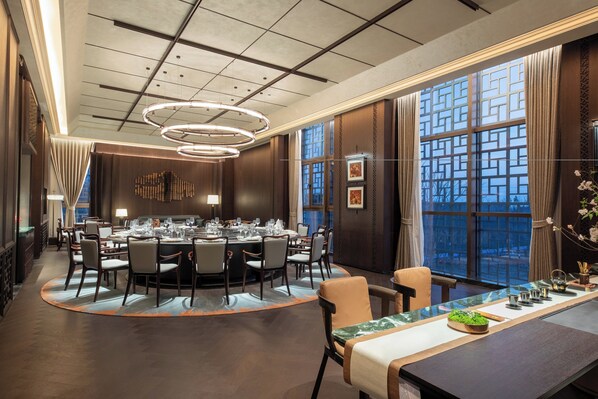 A modern dining area with a round table, chairs, and a long counter with a decorative centerpiece. - Hualuxe Qidong (Nantong)
