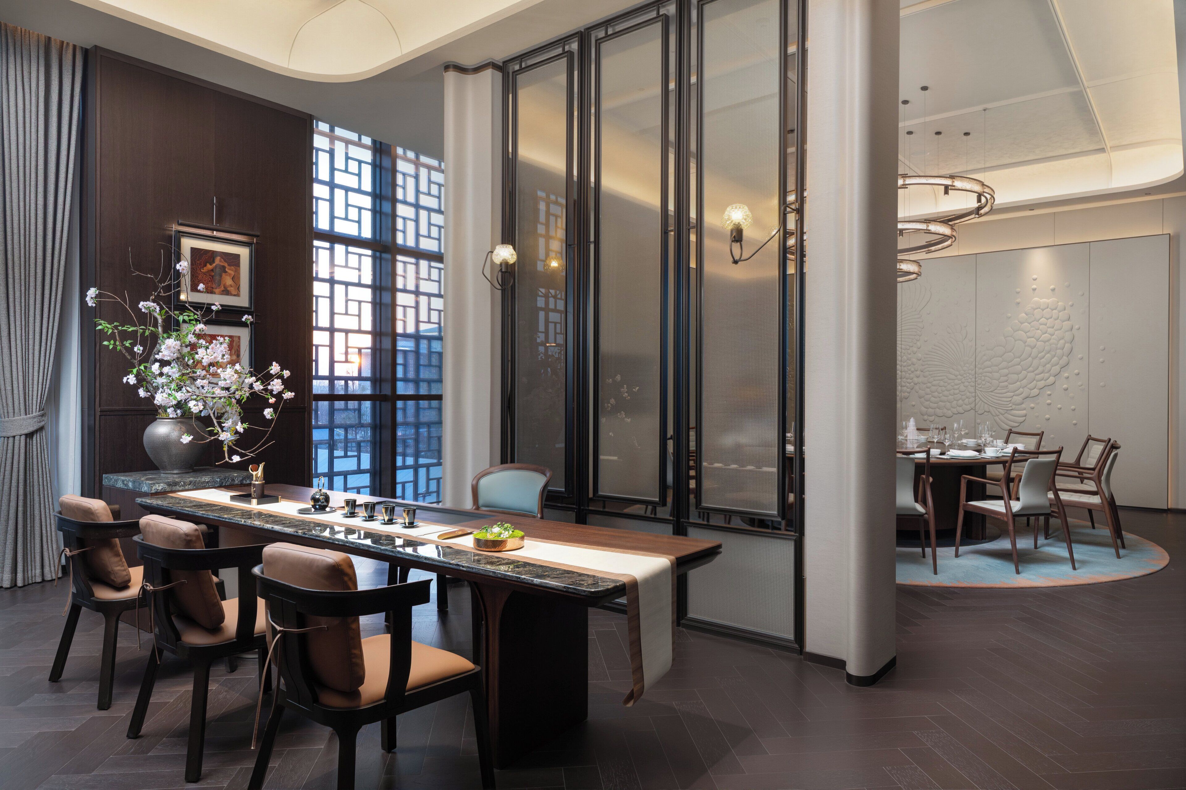 A modern dining area with a long table, chairs, and a vase of flowers.