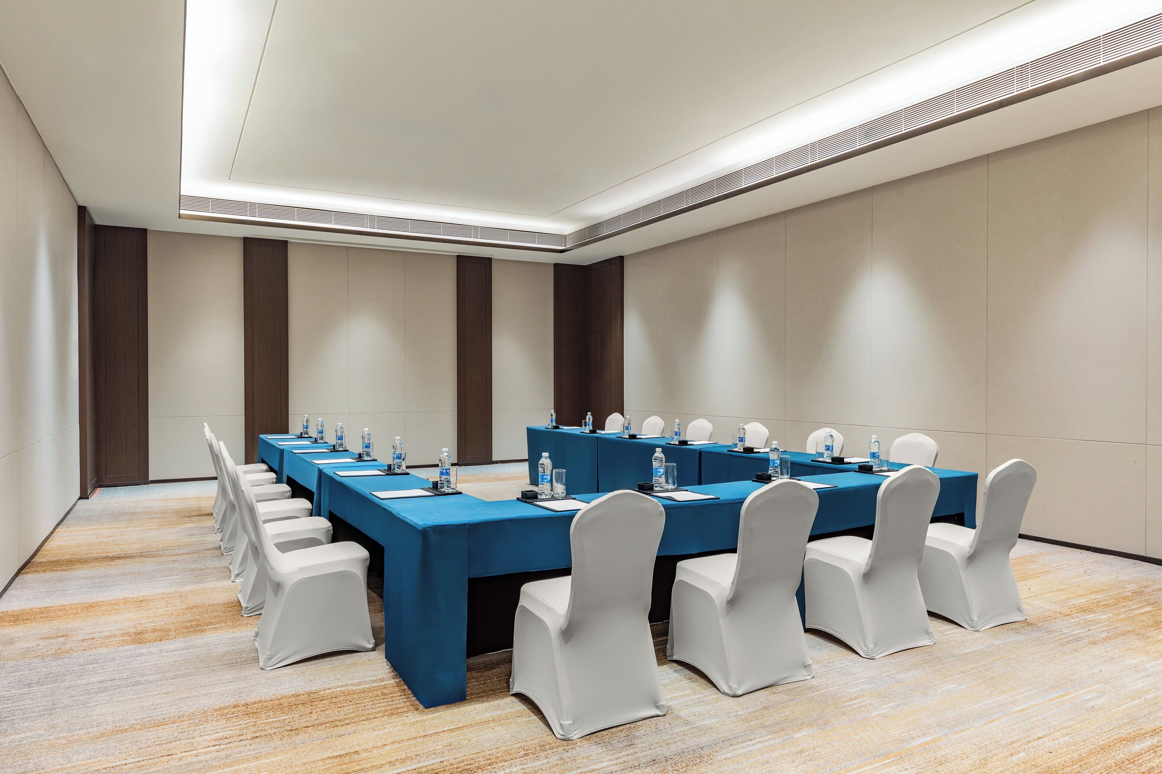 A conference room with a long table, white chairs, and a blue tablecloth.