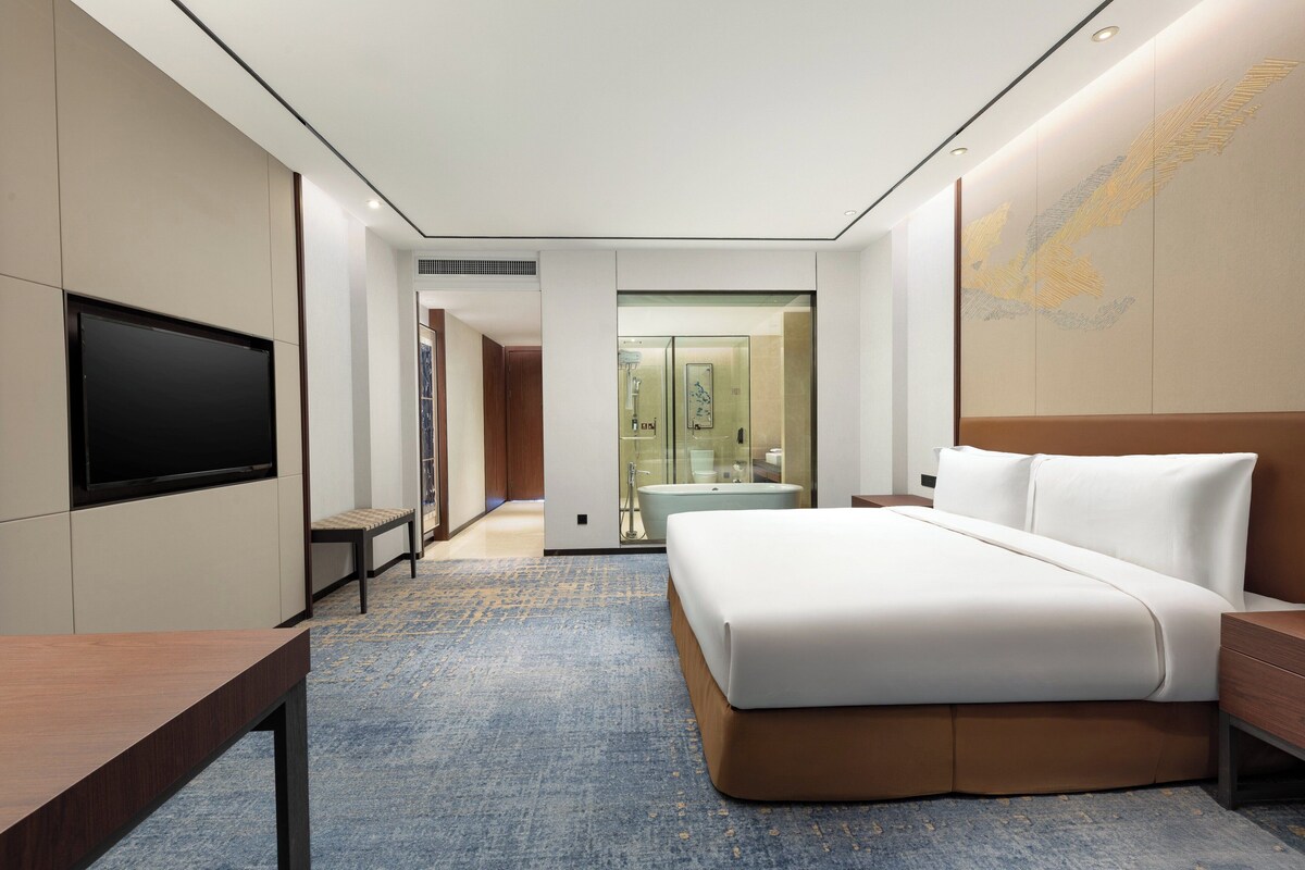 A modern hotel room with a large bed, a flat-screen TV, and a seating area.
