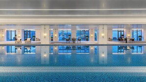 Una piscina interior moderna con agua azul cristalina, sillas de descanso y mesas.