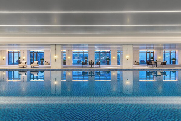 Ein moderner, überdachter Swimmingpool mit klarem, blauem Wasser, Liegestühlen und Tischen.