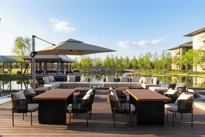 A deck with outdoor seating, a pool, and a view of a building across the water. - Hualuxe Qidong (Nantong)