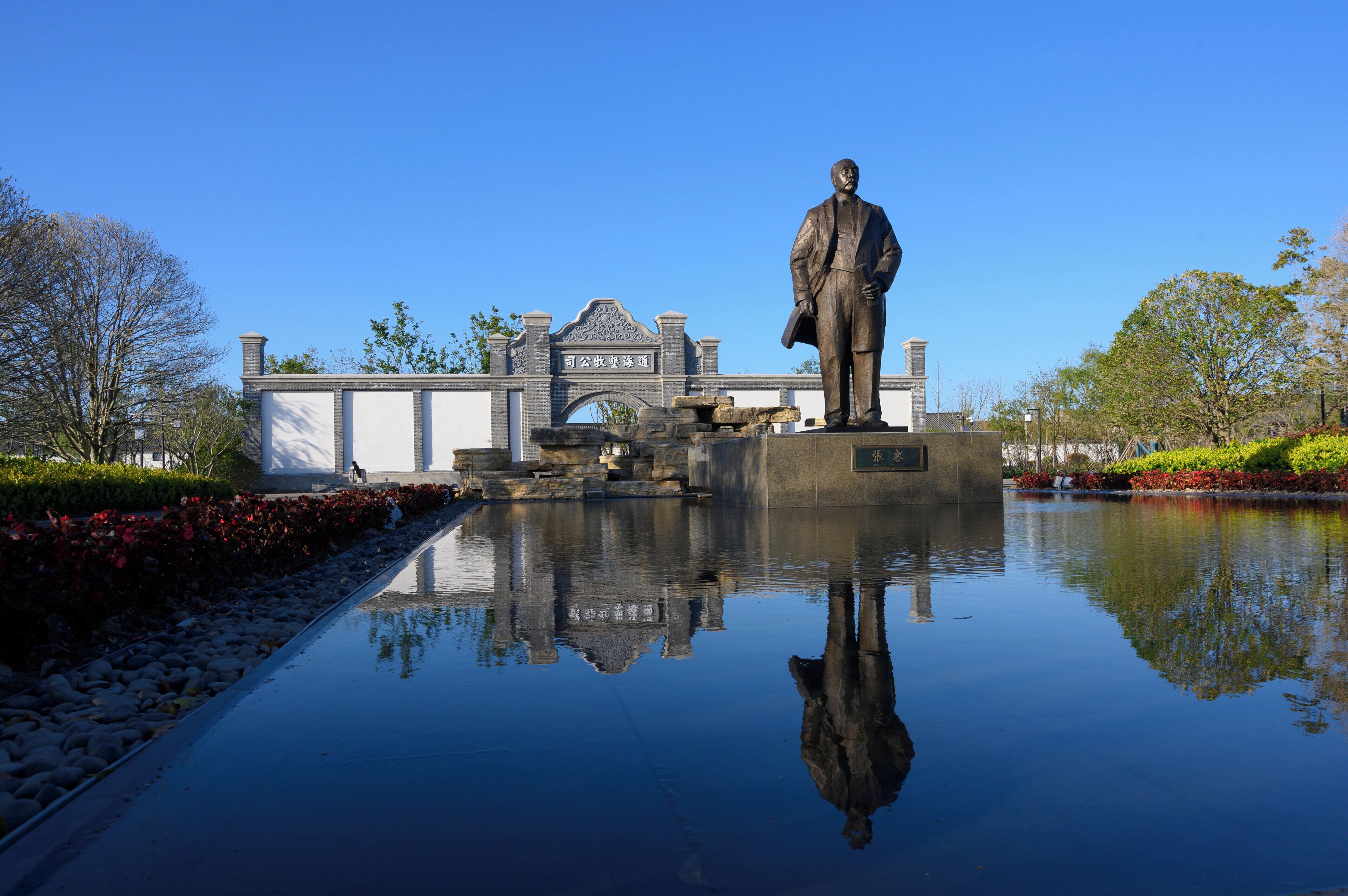 Uma estátua em frente a um edifício com entrada em arco e superfície aquática refletora.
