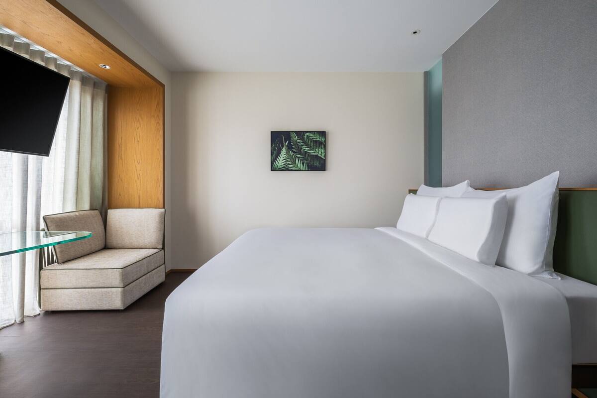 Ein modernes Hotelzimmer mit einem großen Bett, einem Glastisch, einer Couch und einem Wandbild.