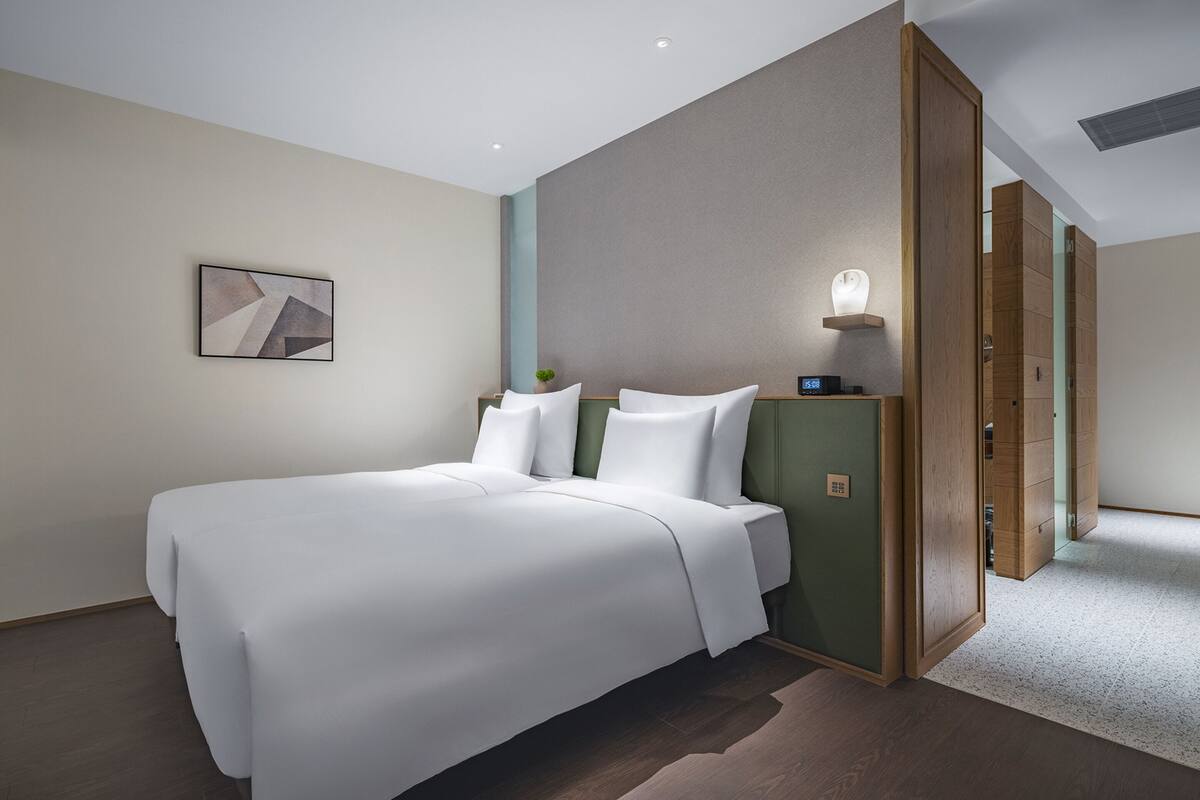 Ein modernes Hotelzimmer mit einem großen Bett, einem Nachttisch mit Lampe und einem Gemälde an der Wand.