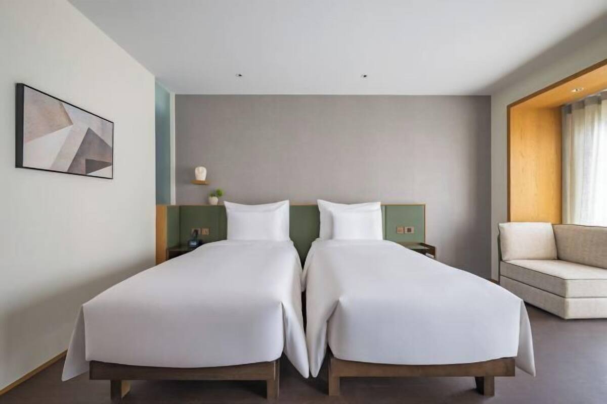 Ein Hotelzimmer mit zwei Einzelbetten, einem Schlafsofa, einem Gemälde und einem Nachttisch mit Lampe.
