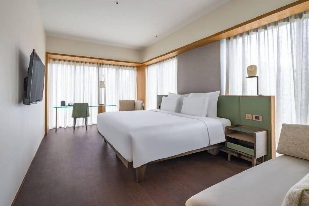 Ein Hotelzimmer mit einem großen Bett, einem Schreibtisch, einem Sessel und einem Fernseher.