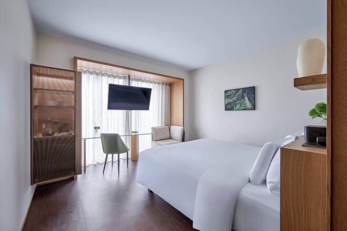 Ein Hotelzimmer mit Bett, Schreibtisch, Sessel, Fernseher und einem Bild an der Wand.