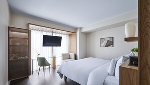 A hotel room with a large bed, a television, a small table with a chair, and a decorative vase on a shelf. - Humble Boutique Hotel (Taipei)