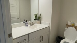 A modern bathroom with a white vanity, a large mirror, a sink, and a toilet.