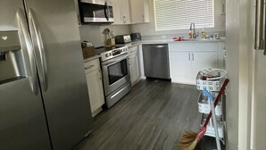 A modern kitchen with stainless steel appliances, white cabinets, and a window with blinds.