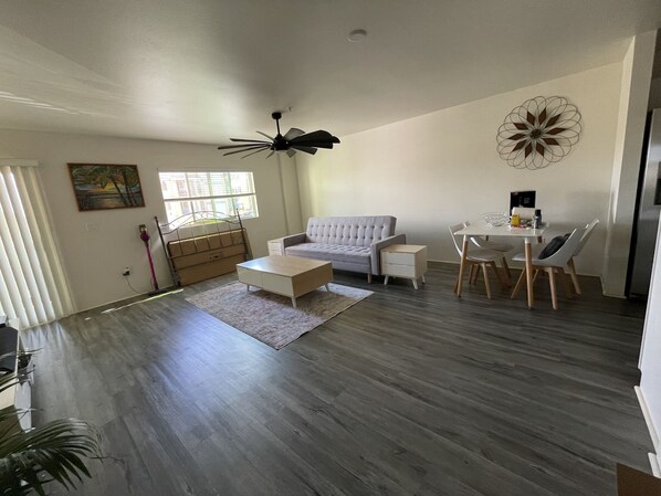 A spacious living area with a grey sofa, a coffee table, and a dining table with chairs.