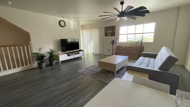 A modern living room with a flat-screen TV, a sofa, a coffee table, and a ceiling fan.