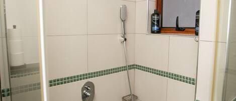 A small, tiled shower area with a handheld showerhead, a wall-mounted faucet, and a window with a wooden frame.