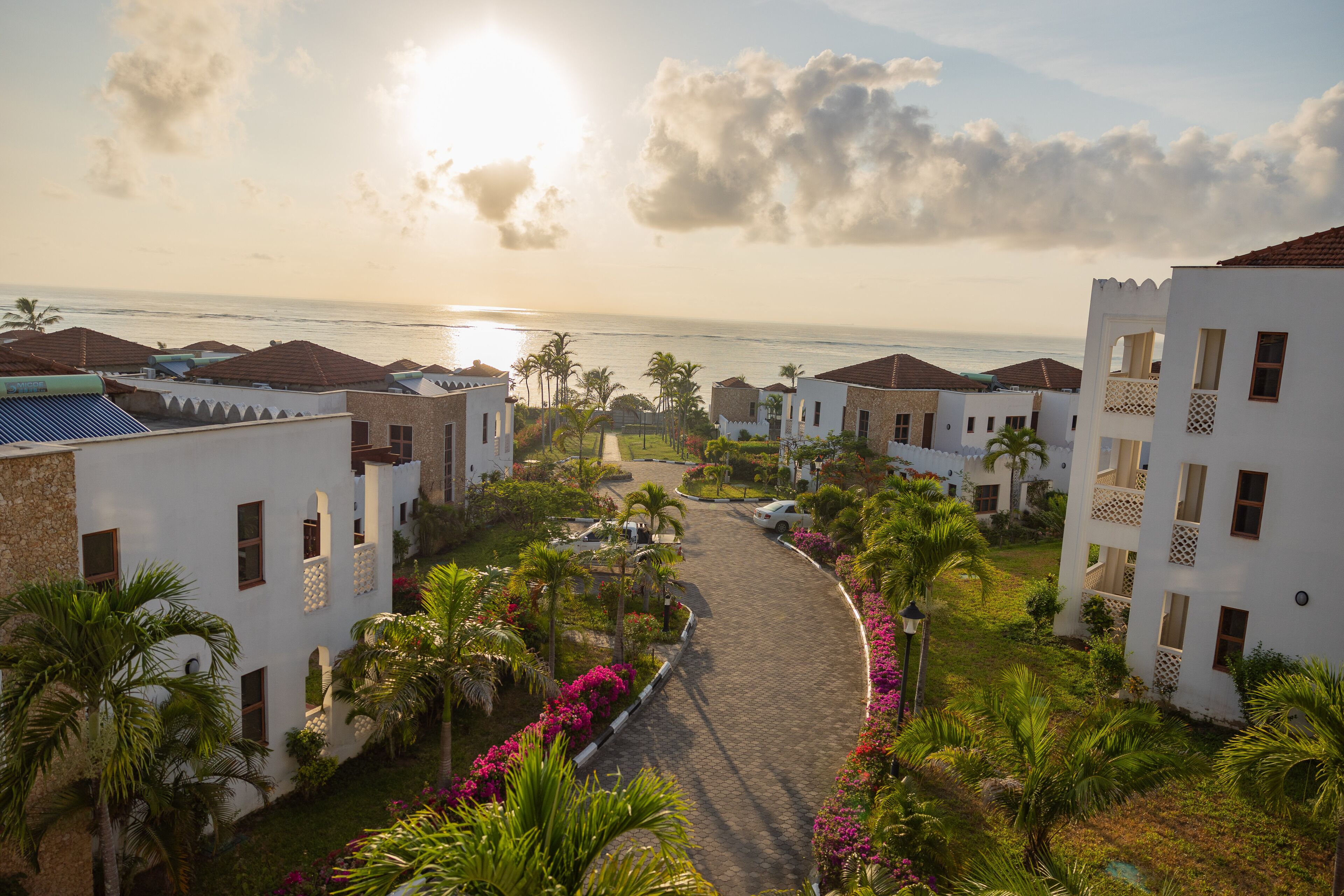 A resort with a paved pathway leading to the beach, surrounded by palm trees and buildings with balconies.