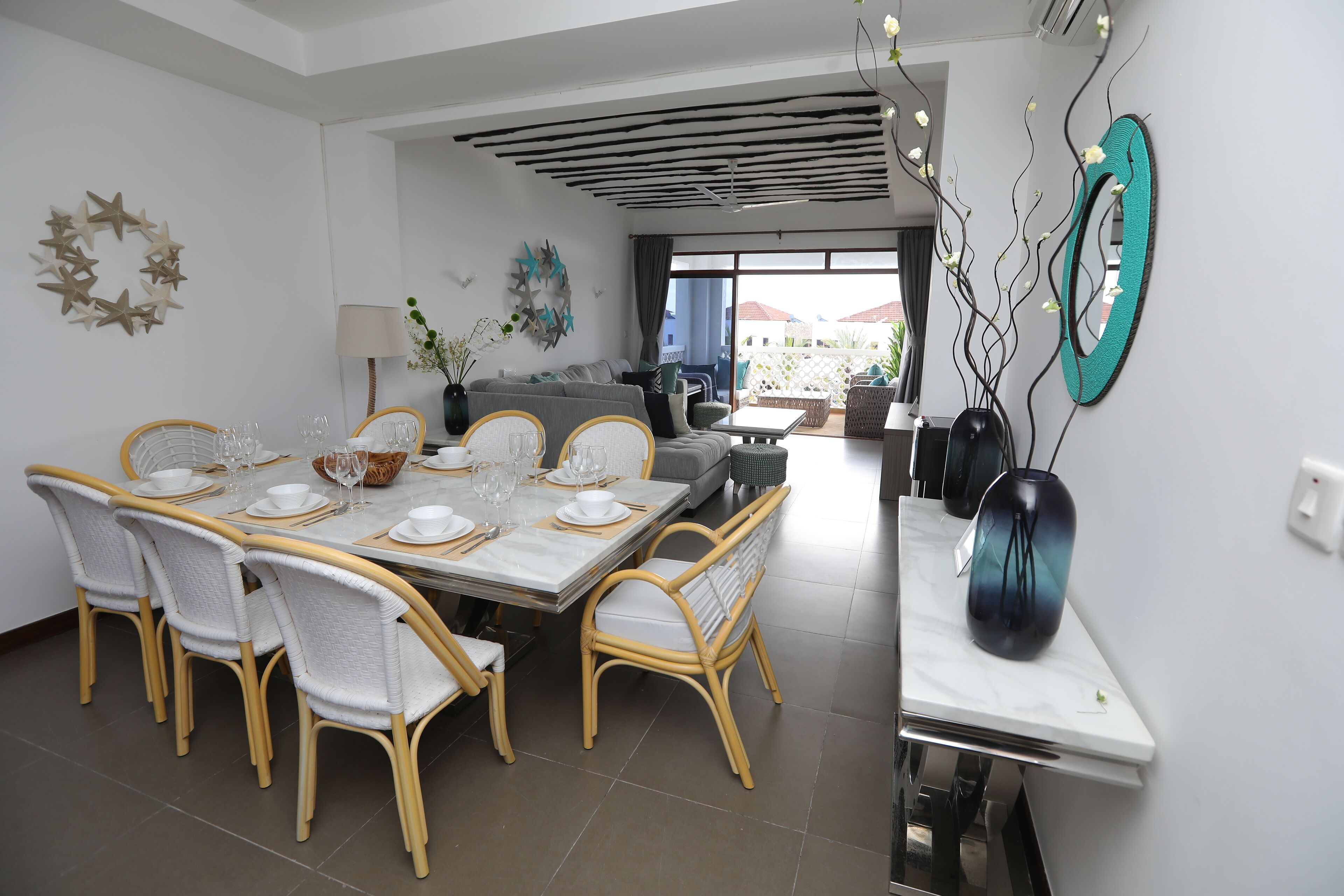 A dining area with a table set for six, surrounded by wicker chairs, a sofa, and a coffee table.