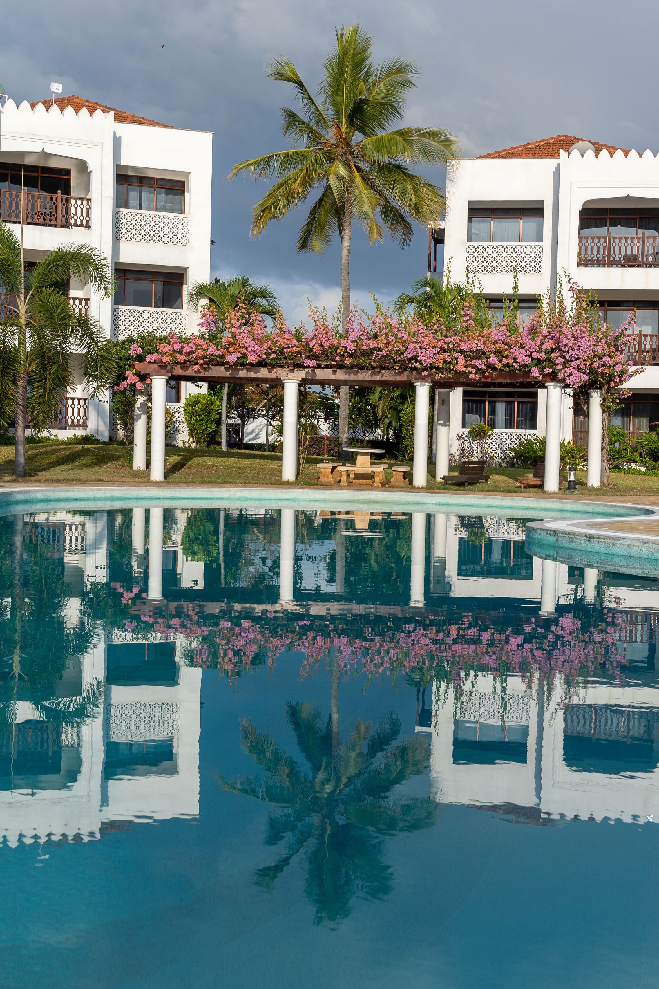 A pool with a reflection of a building and palm trees.