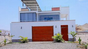 A modern two-story building with a garage, solar panels, and a desert landscape in the background.