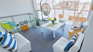 A modern living room with a white sofa, a dining table, and a hanging chair.