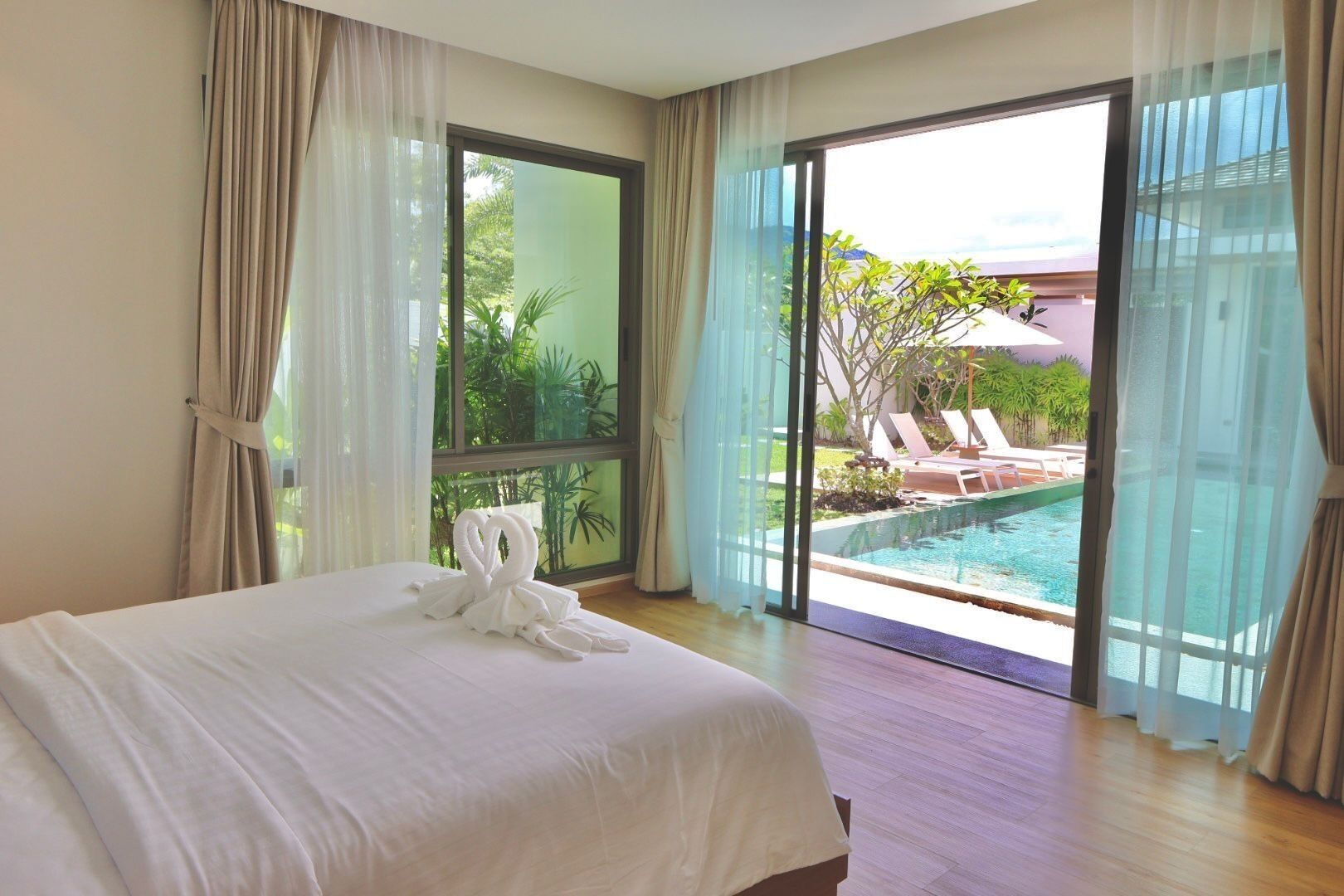 Ein Hotelzimmer mit Bett, Blick auf einen Swimmingpool und einem Balkon mit Sitzgelegenheit.