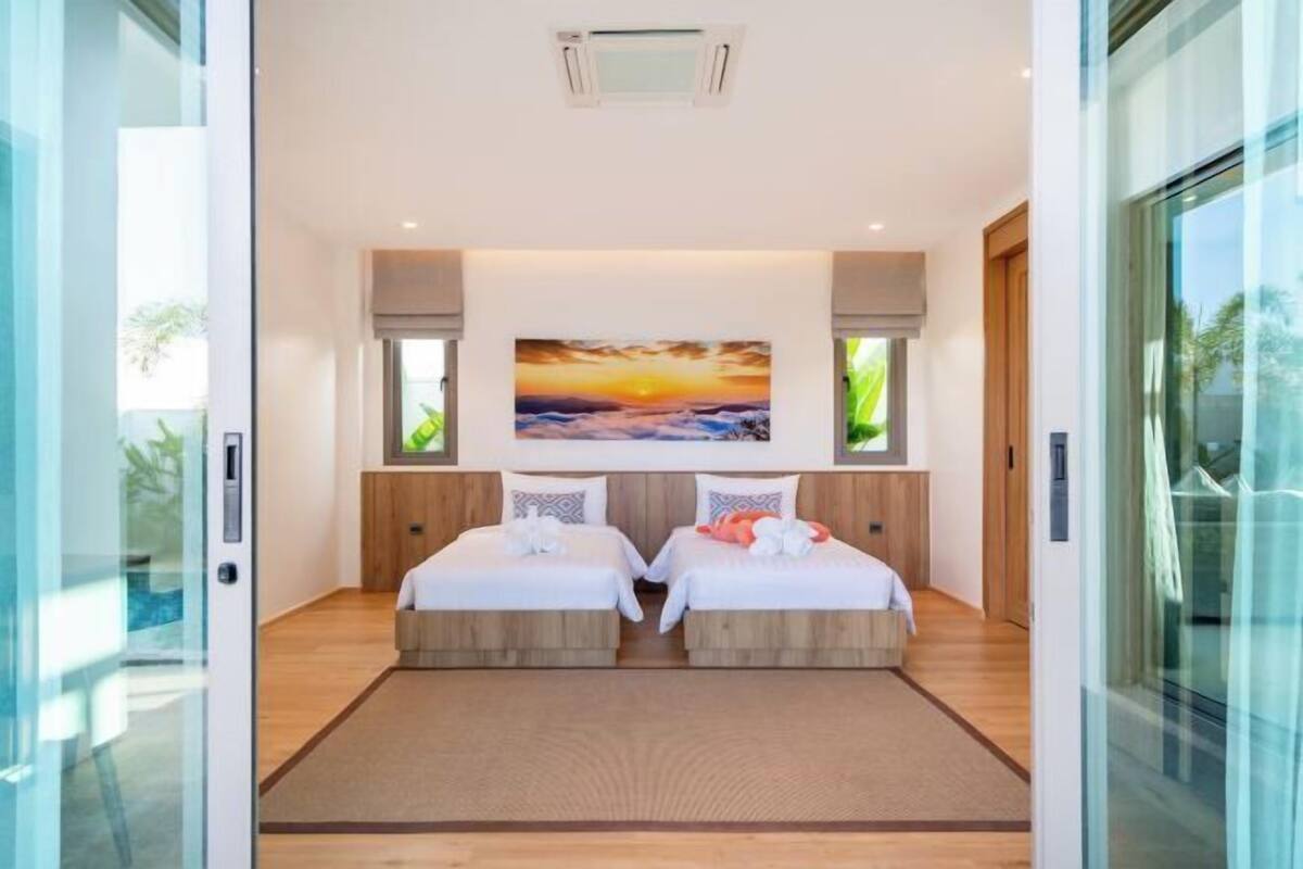 A modern hotel room with two beds, a large painting of a sunset, and a glass door leading to a pool.