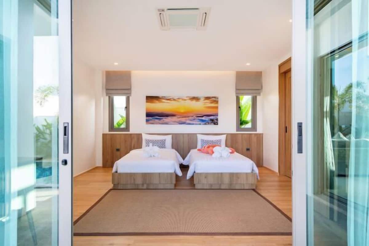 Una habitación de hotel moderna con dos camas, un cuadro grande de un atardecer y un vidrio corredizo que da a una piscina.