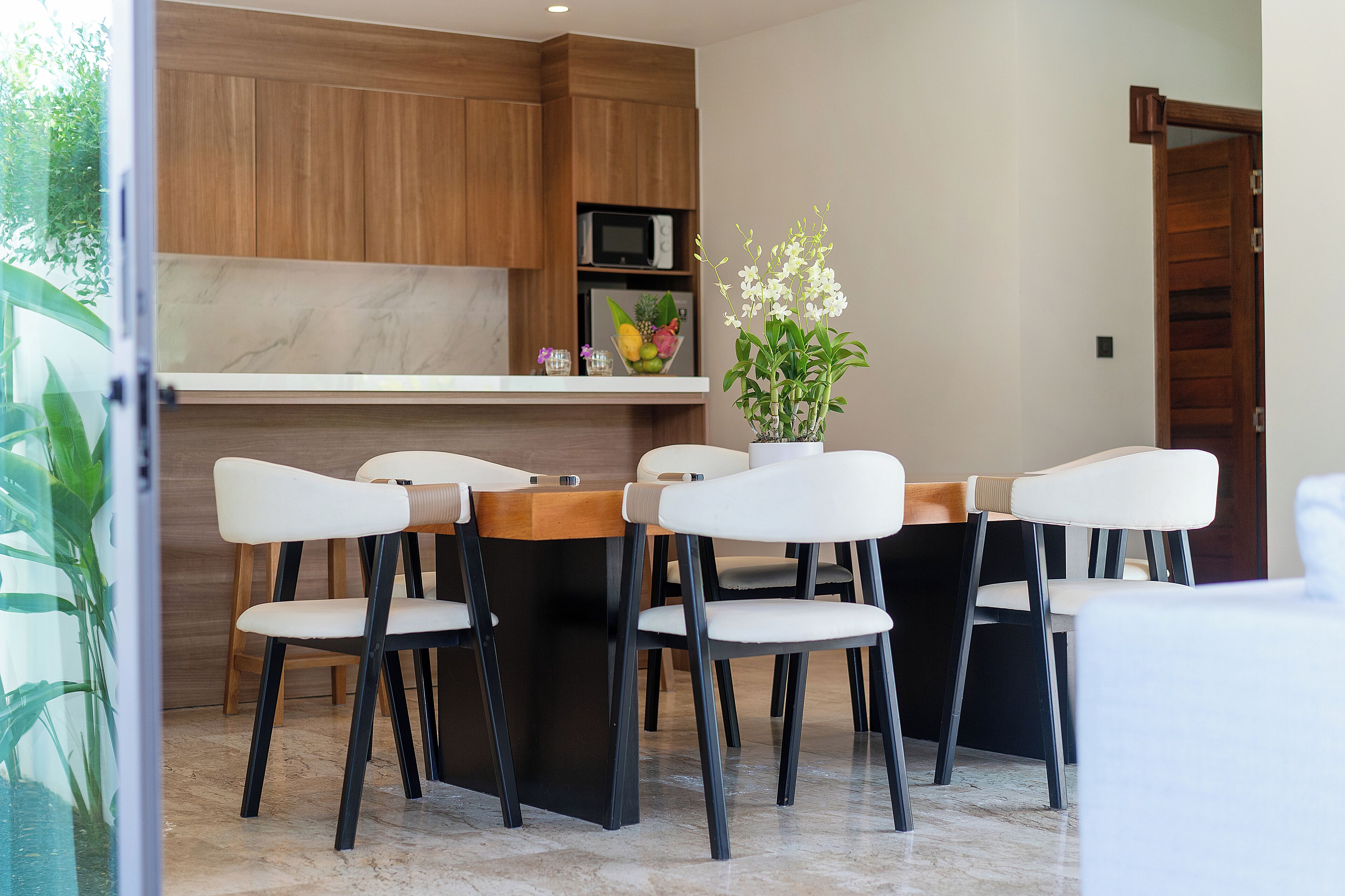 A modern kitchen with wooden cabinets, a marble countertop, and a dining area with white chairs and a wooden table.