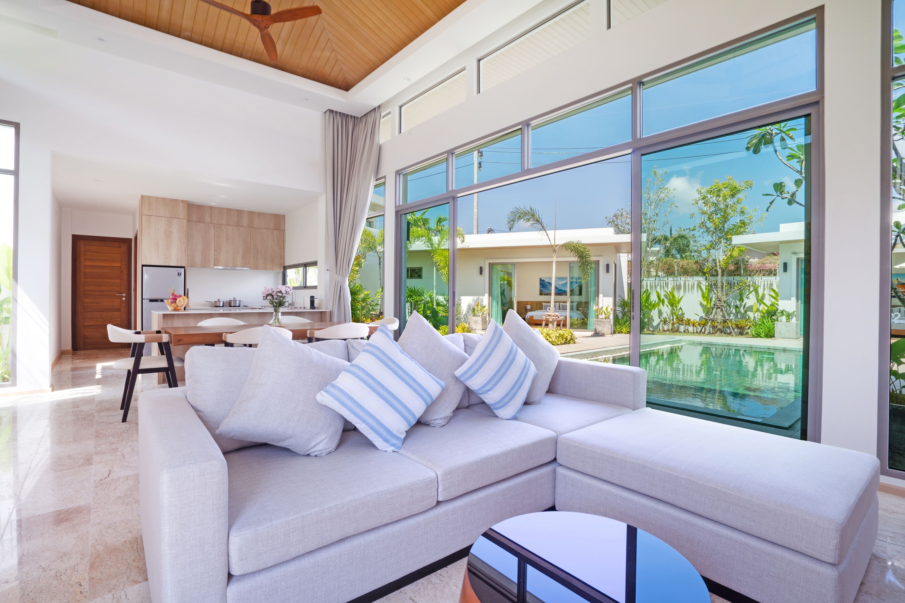 A modern living room with a large sectional sofa, a dining area, and a view of a swimming pool and greenery.