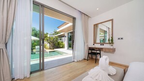 Una habitación de hotel moderna con un amplio ventanal corredera que da a una piscina, un escritorio de madera, una cama con bata blanca y un espejo grande.