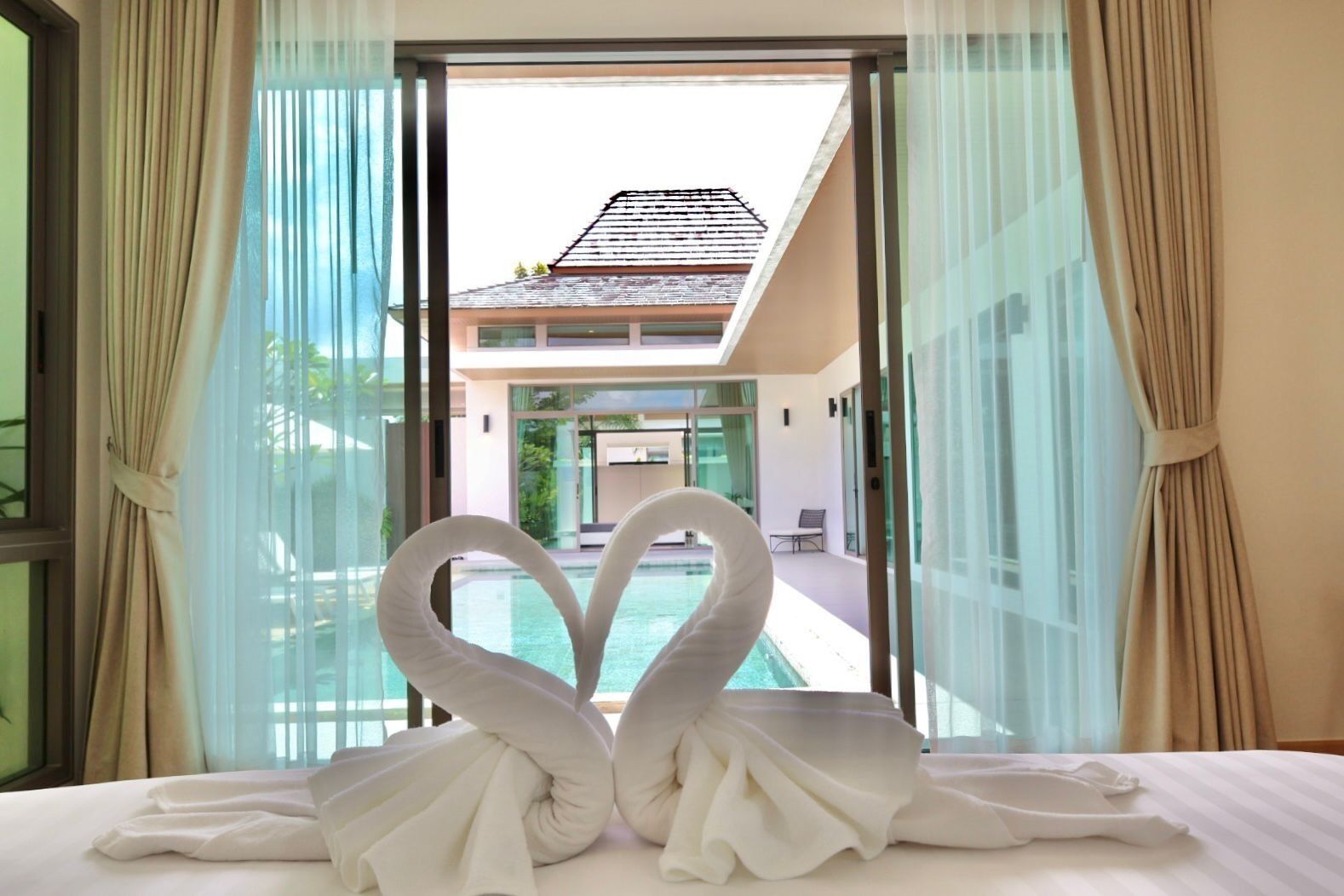 A hotel room with a bed, a window with curtains, and a view of a swimming pool and building.