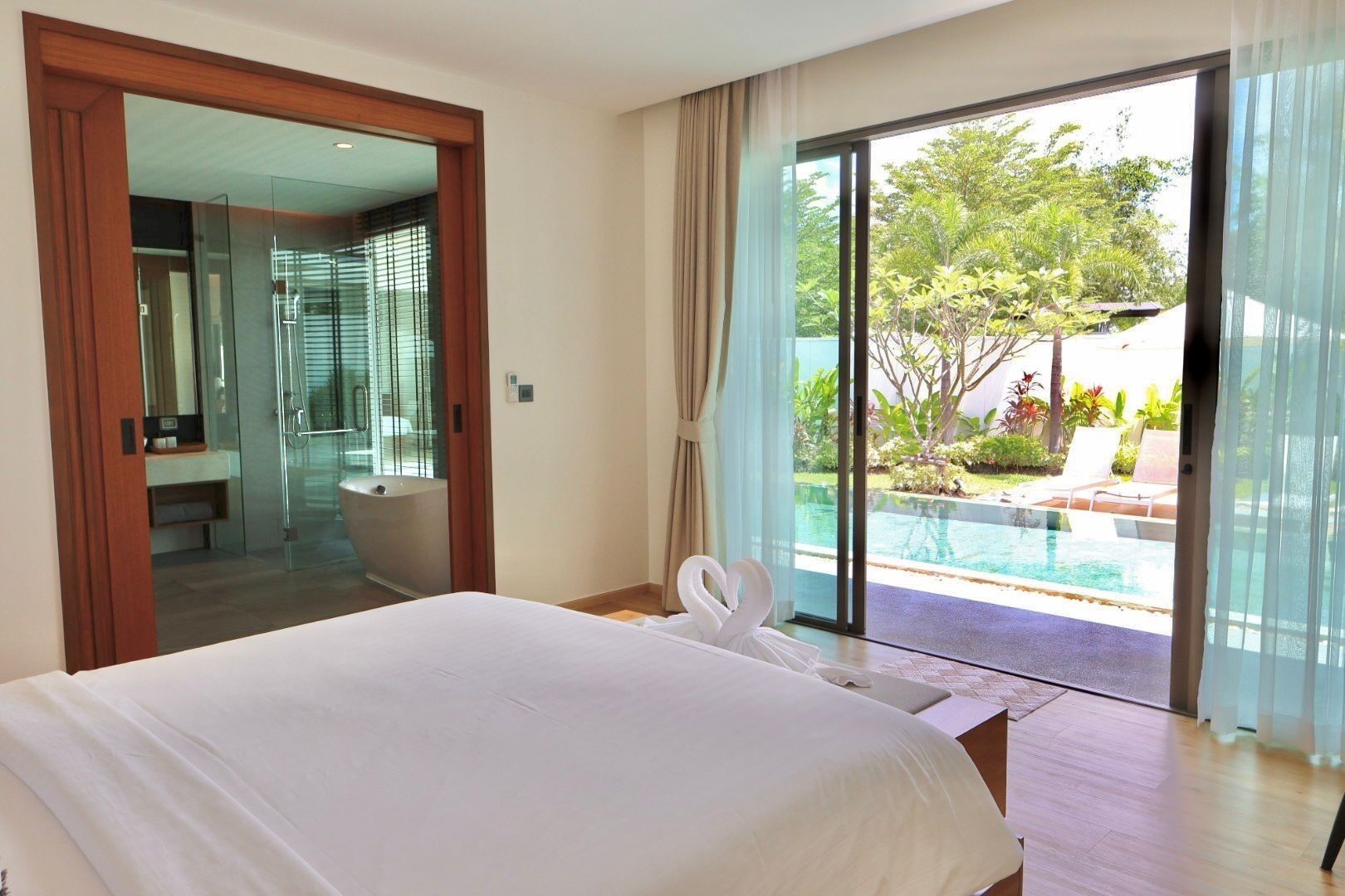 A hotel room with a large bed, a bathroom with a glass shower enclosure, and a view of a swimming pool.