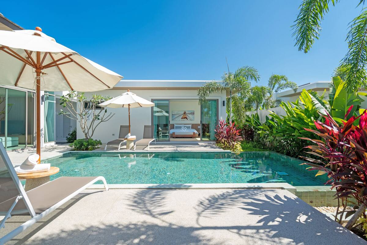 A modern pool area with lounge chairs, umbrellas, and a view of a bedroom with a bed and artwork.
