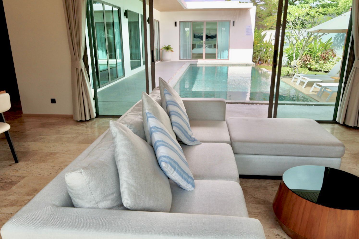 Una sala de estar moderna con un sofá seccional grande, una mesa redonda de centro y vista a una piscina y zona de estar al aire libre.